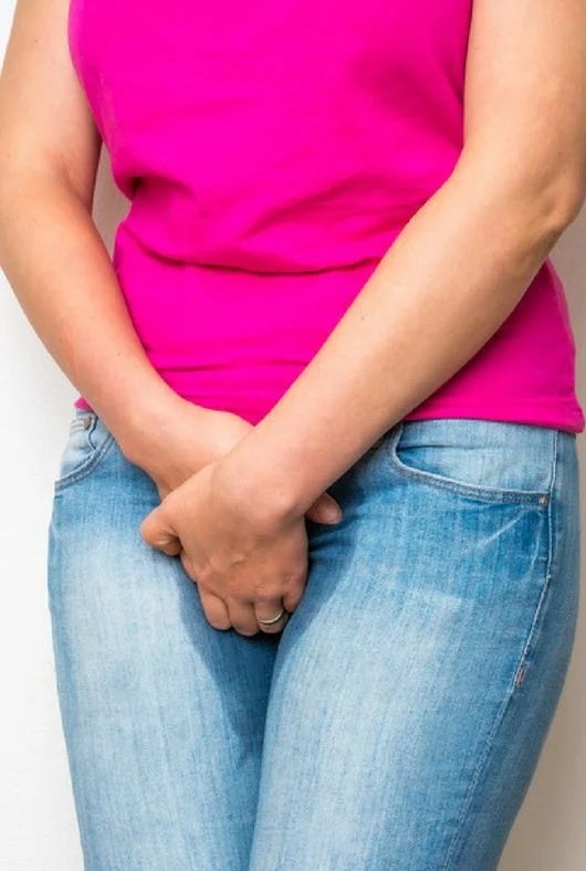 Mulher com as mãos sobre o abdômen, representando os sintomas da incontinência urinária