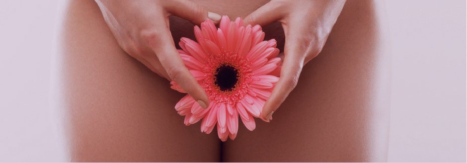 Mãos em formato de coração segurando uma flor, representando a região íntima feminina